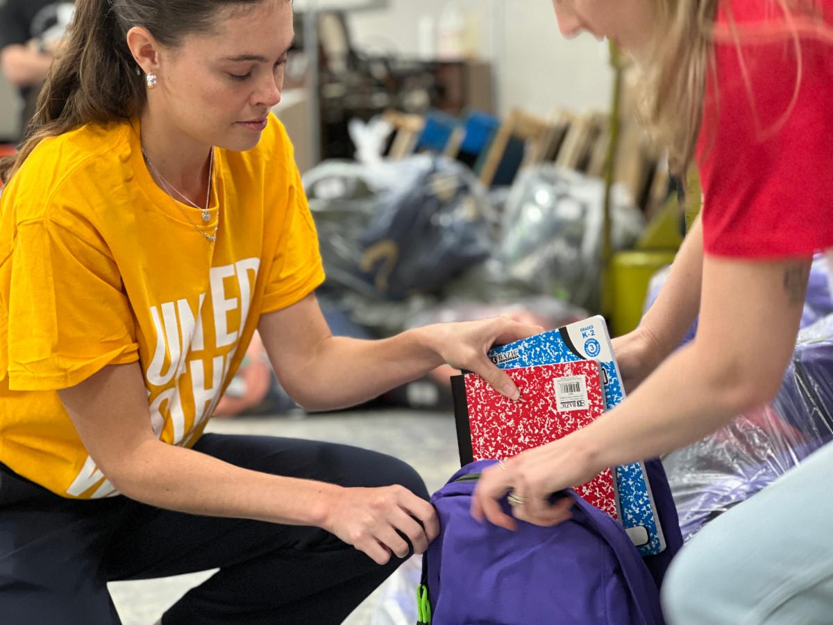 United Way employees stuff a backpack with notebooks for children in need