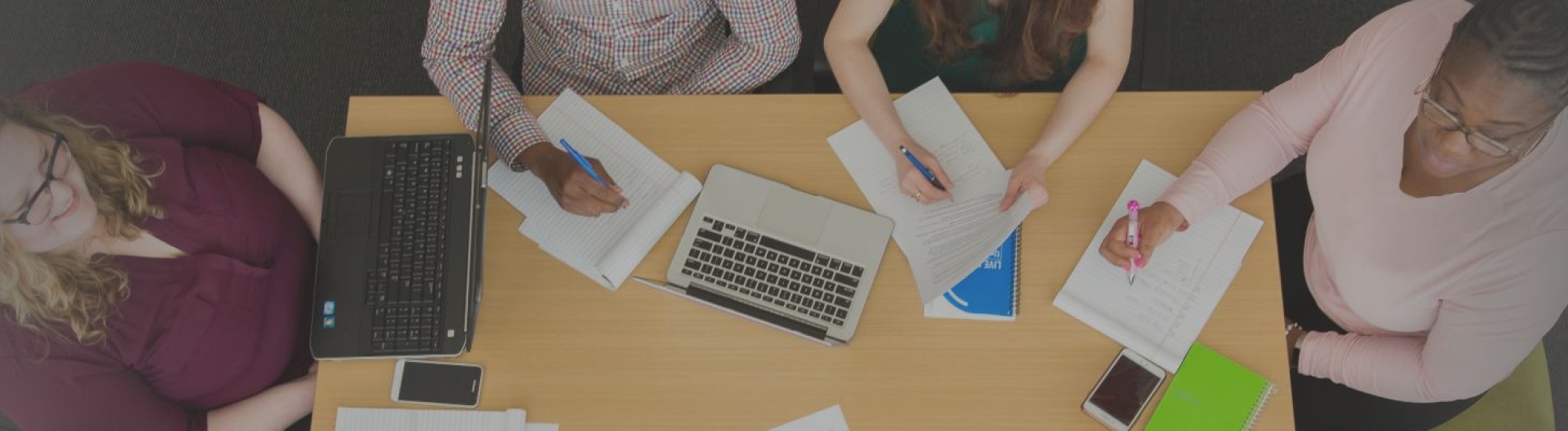 Aerial view of people sitting around a desk with paperwork and laptops