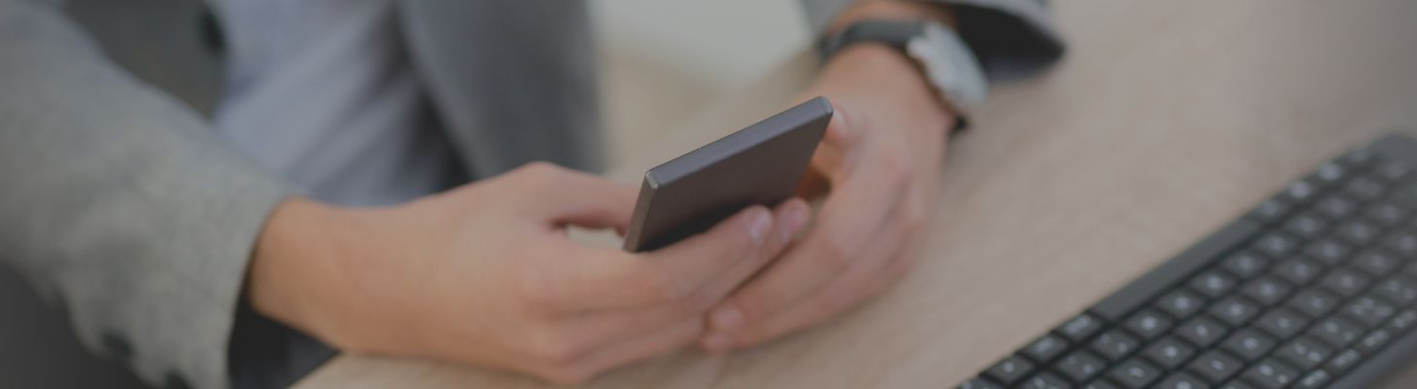 close-up photo of someone holder a cell phone with a keyboard in front of them